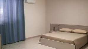 A bedroom with a bed, a nightstand, a lamp, and a window with curtains.