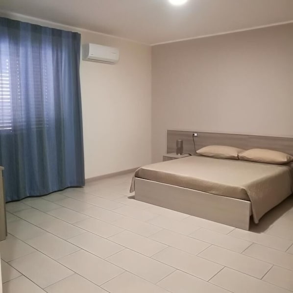 Une chambre à coucher avec un lit, une table de chevet, une lampe et une fenêtre avec des rideaux.