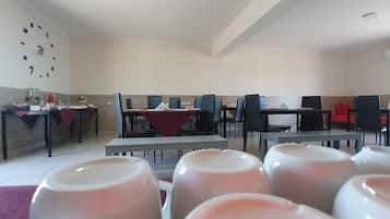 Un comedor con varias mesas y sillas, un reloj en la pared y un mantel rojo sobre una de las mesas.