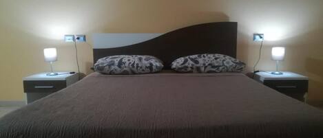 Una cama con cabecera oscura, dos almohadas estampadas y lámparas de noche en mesitas.