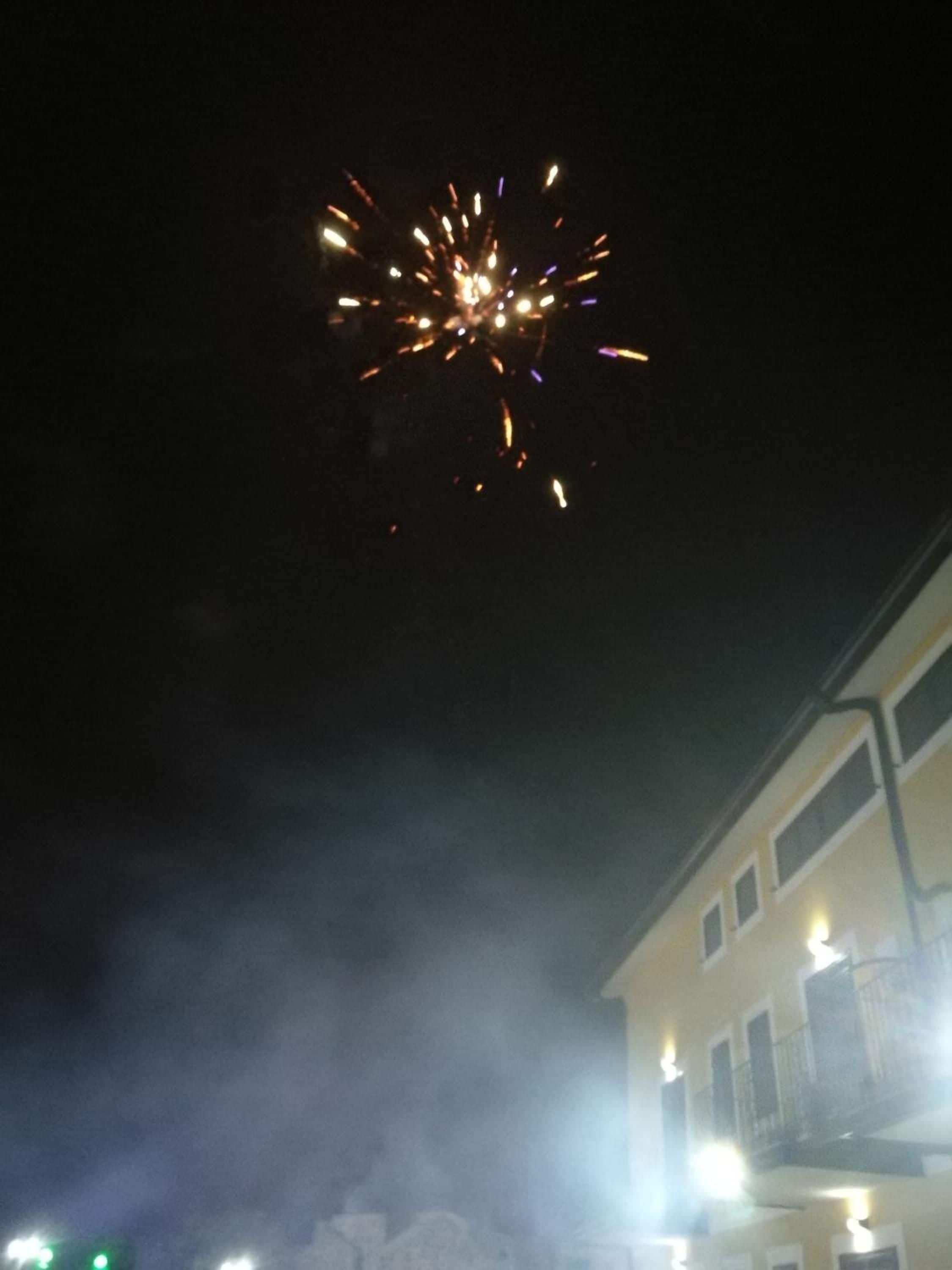 A building with multiple windows and balconies, under a night sky with visible fireworks.