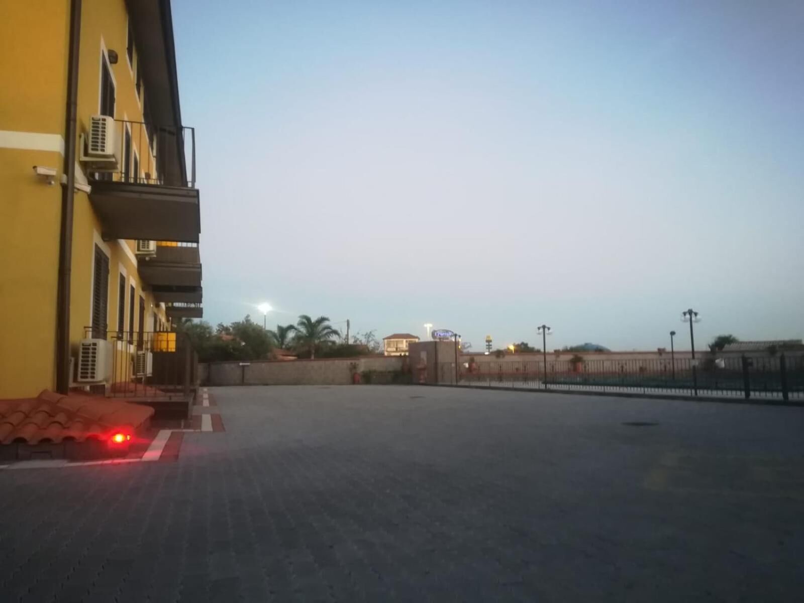 Un edificio con fachada amarilla, unidades de aire acondicionado y un área pavimentada en la parte delantera.
