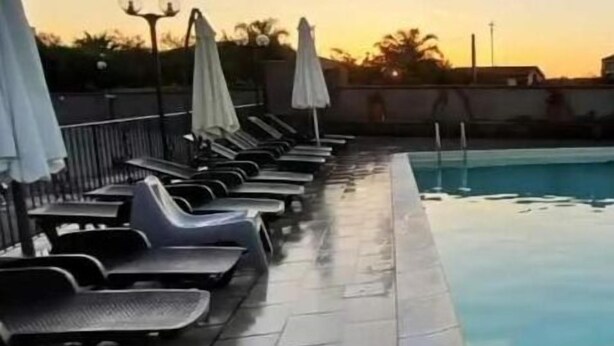 A poolside area with lounge chairs and umbrellas, a tiled floor, and a clear view of the sky.