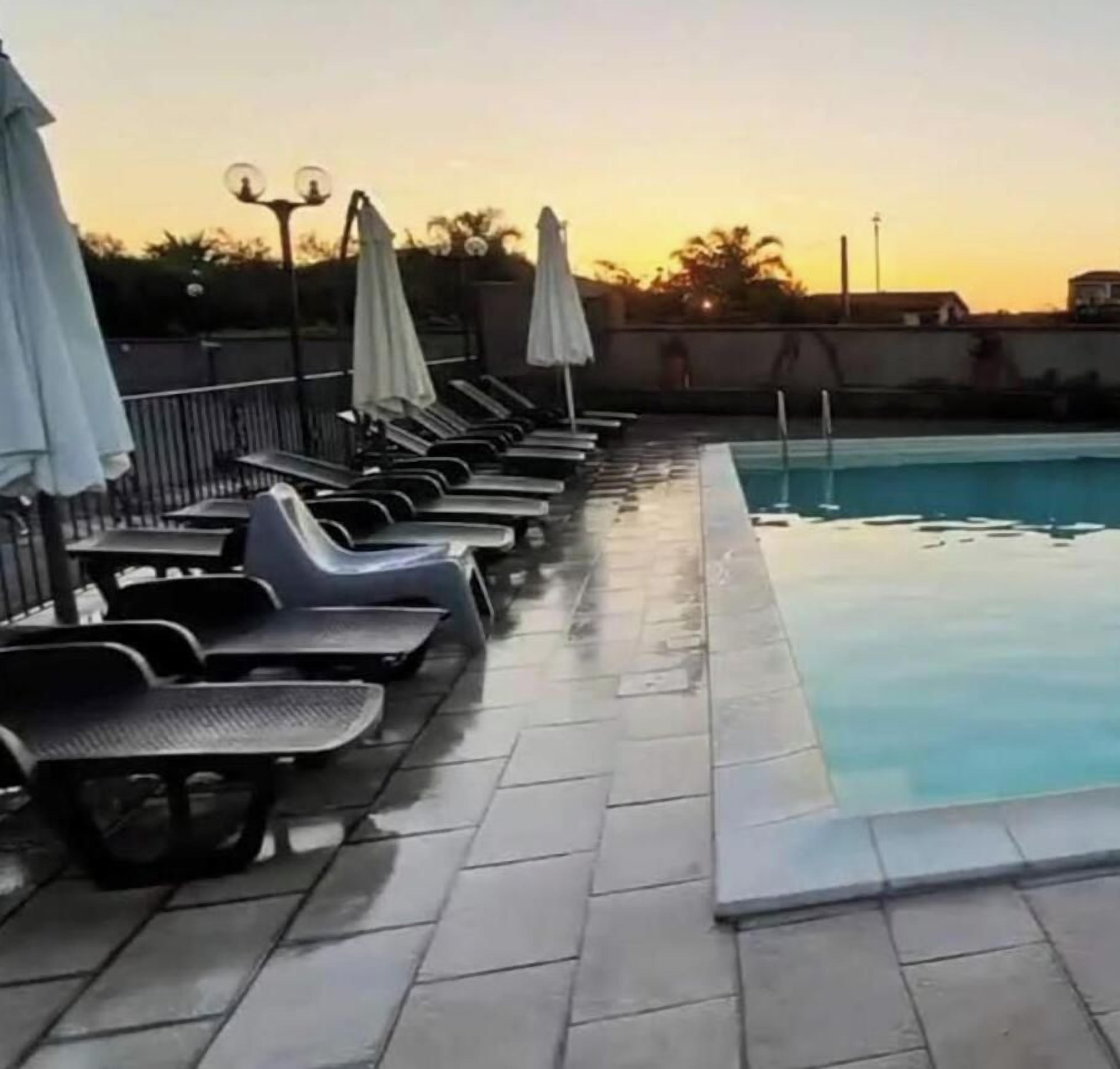 Una piscina con sillas de descanso y sombrillas, rodeada de un solárium con baldosas.