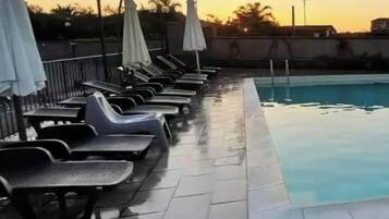 Una piscina con sillas de descanso y sombrillas, rodeada de un solárium con baldosas.