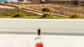 Una mesa con dos copas de vino, una botella y un frutero con uvas, melocotones y una pera.