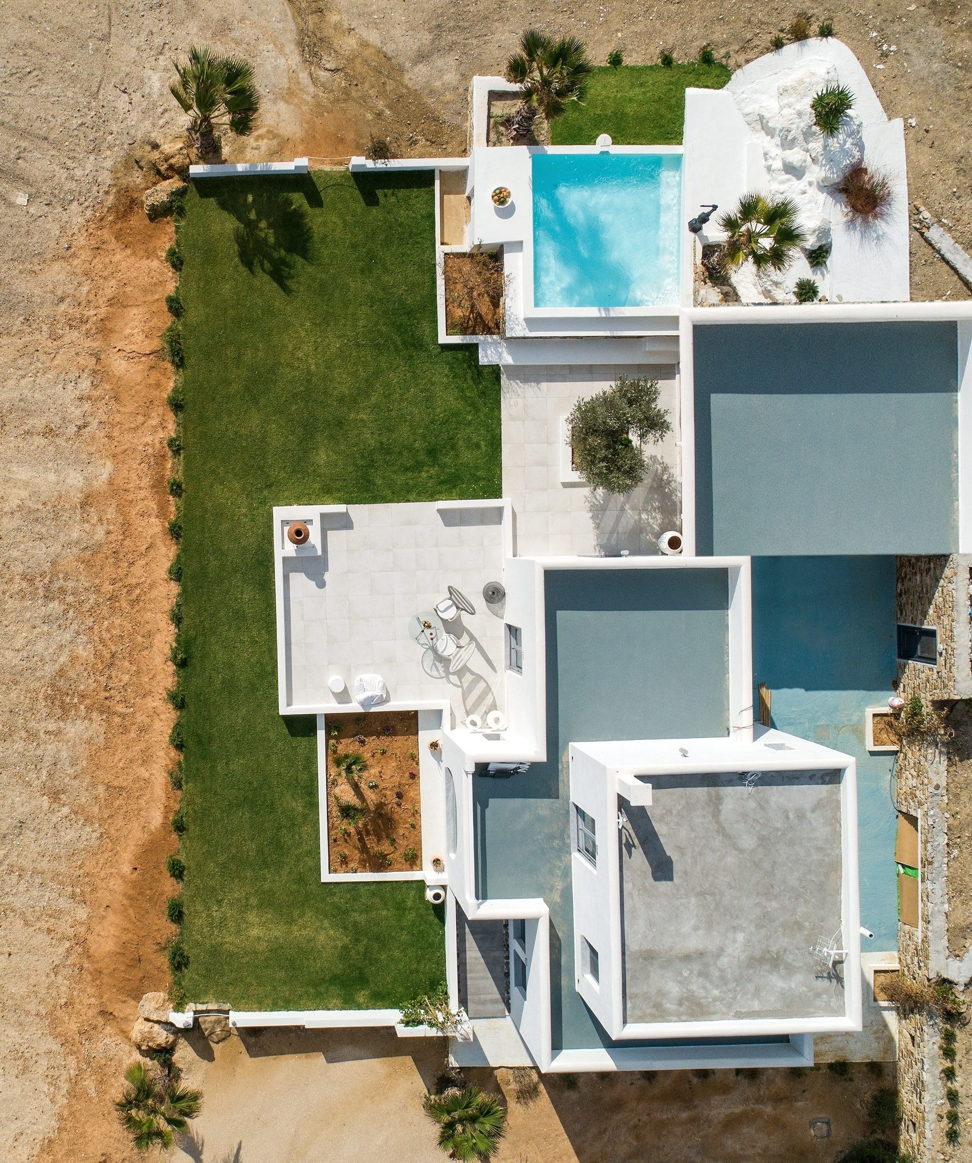 An aerial view of a modern house with a swimming pool, a patio, and a well-maintained lawn.