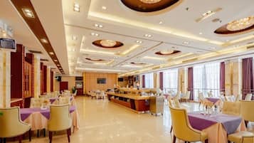 A spacious hotel dining area with multiple tables and chairs, a central bar, and large windows.