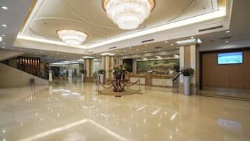 A spacious lobby with a polished marble floor, a reception desk, and a large chandelier.