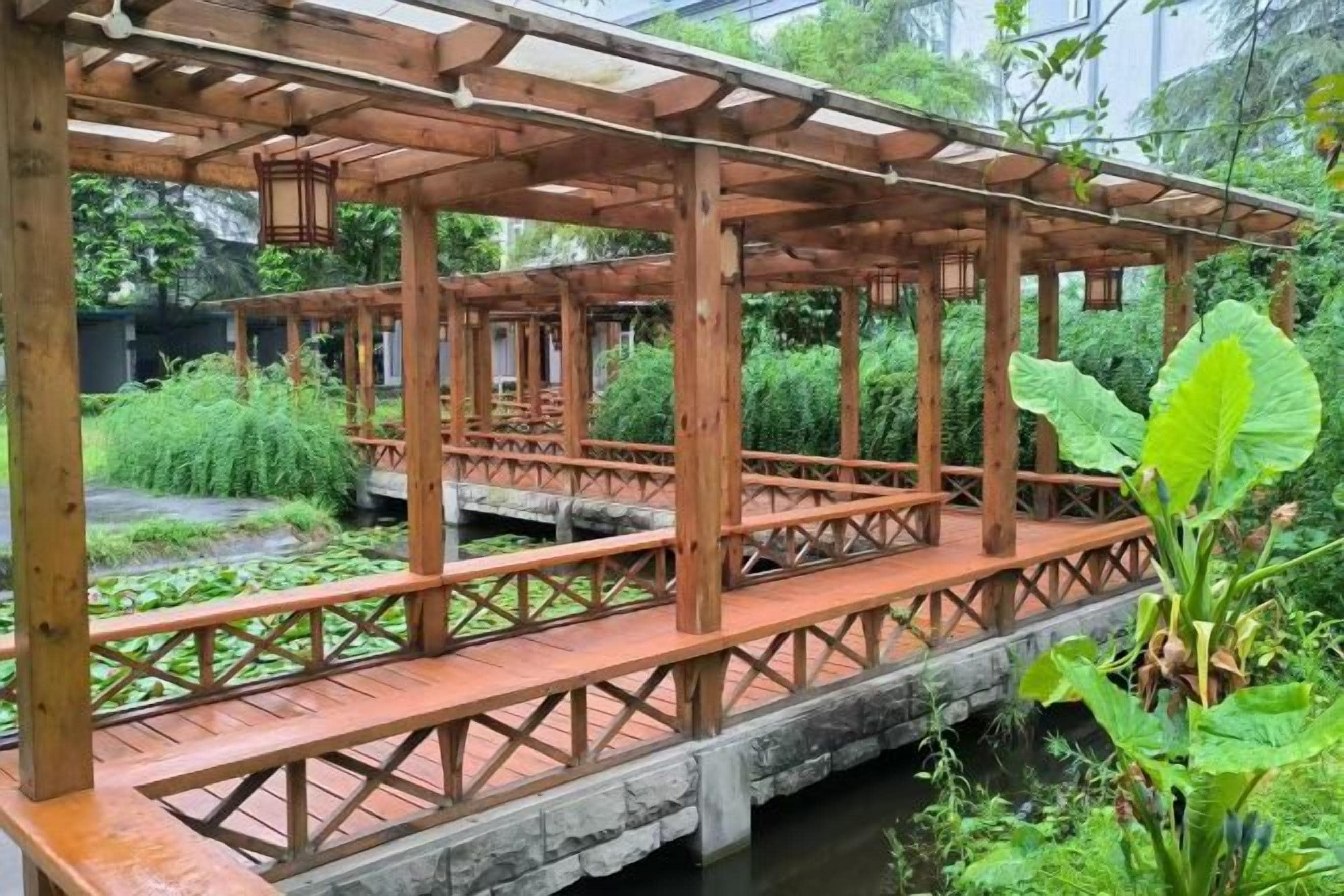 Un puente de madera con techo que cruza un cuerpo de agua, rodeado de exuberante vegetación.