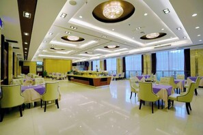 Un amplio comedor de hotel con mesas y sillas redondas, una barra central y un candelabro.