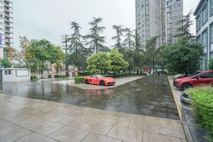 Zona residencial con un coche deportivo rojo estacionado en la calle, rodeada de edificios altos y árboles.