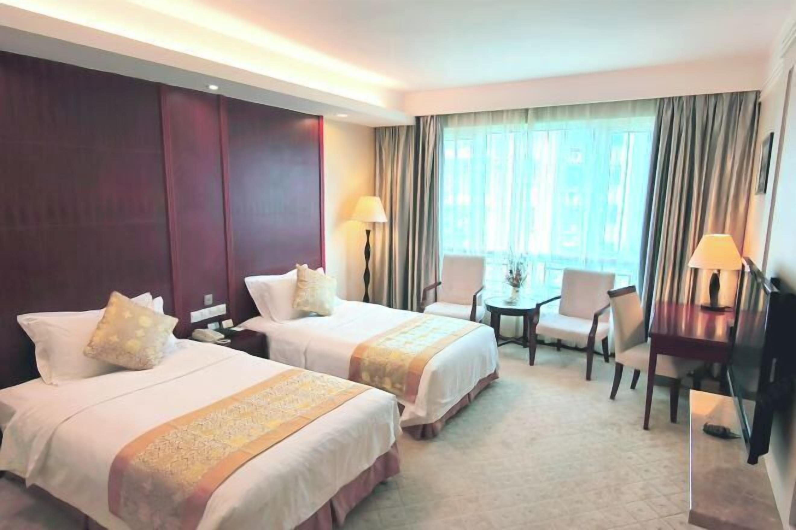 A hotel room with two beds, a desk, a chair, and a TV.