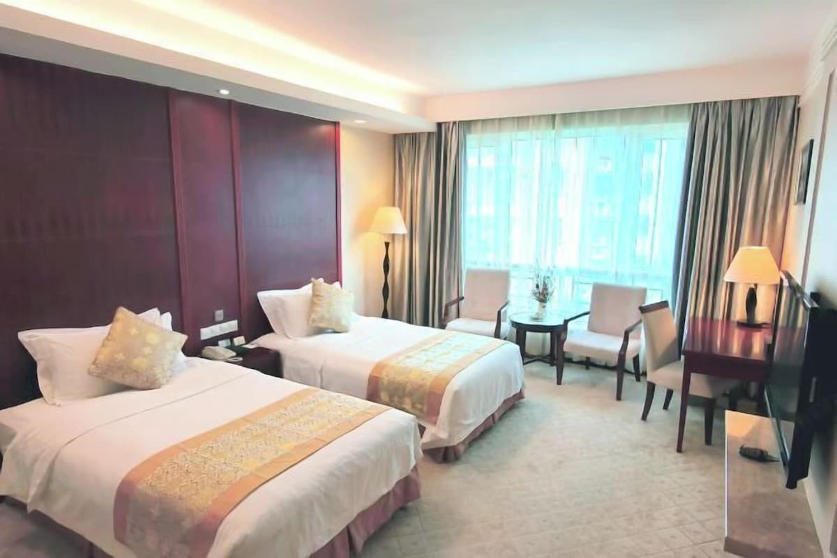 A hotel room with two beds, a desk, a chair, and a TV.
