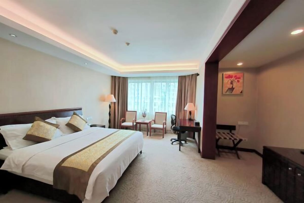 A hotel room with a large bed, a desk, two chairs, and a small table.
