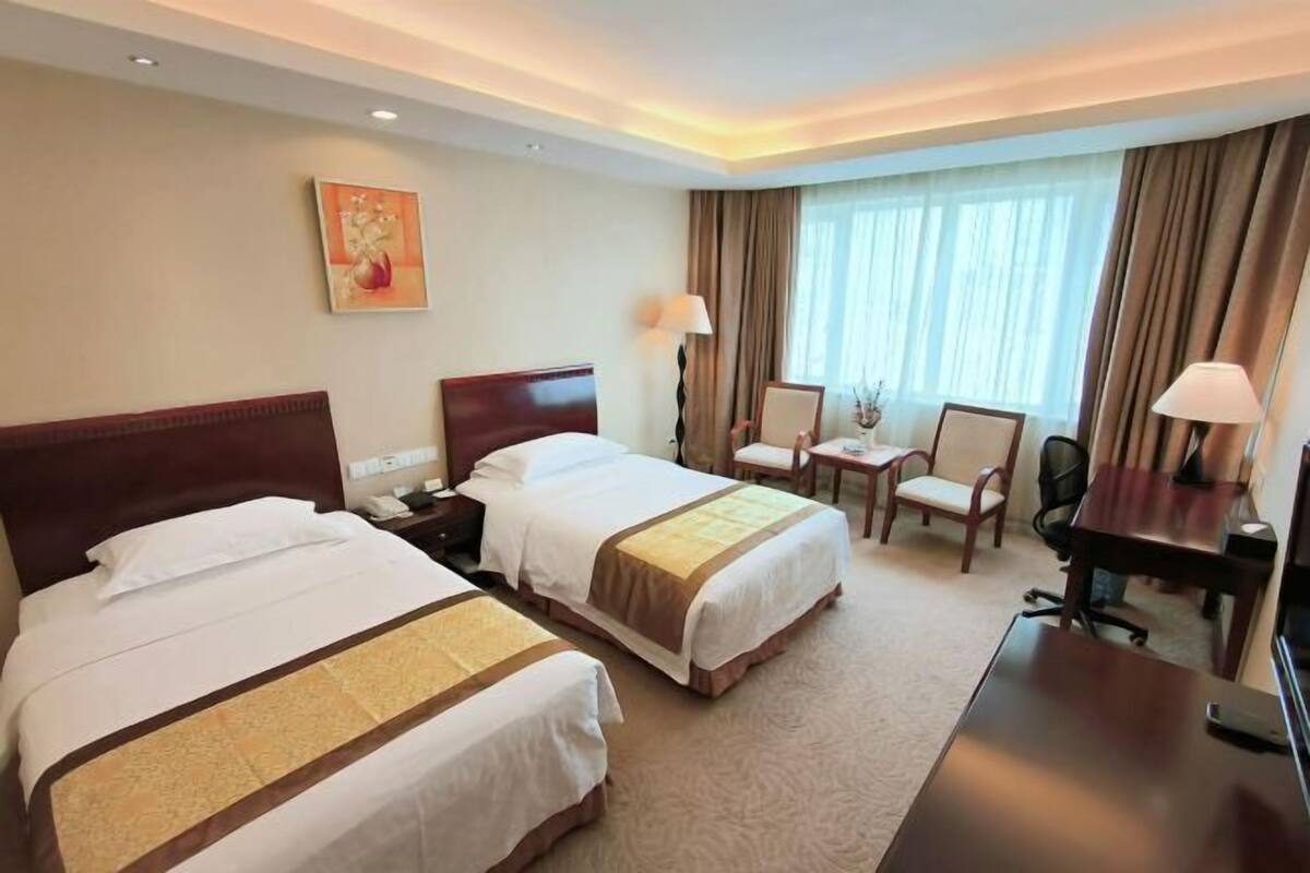 Une chambre d’hôtel avec deux lits, un bureau, une chaise, une lampe et un tableau au mur.