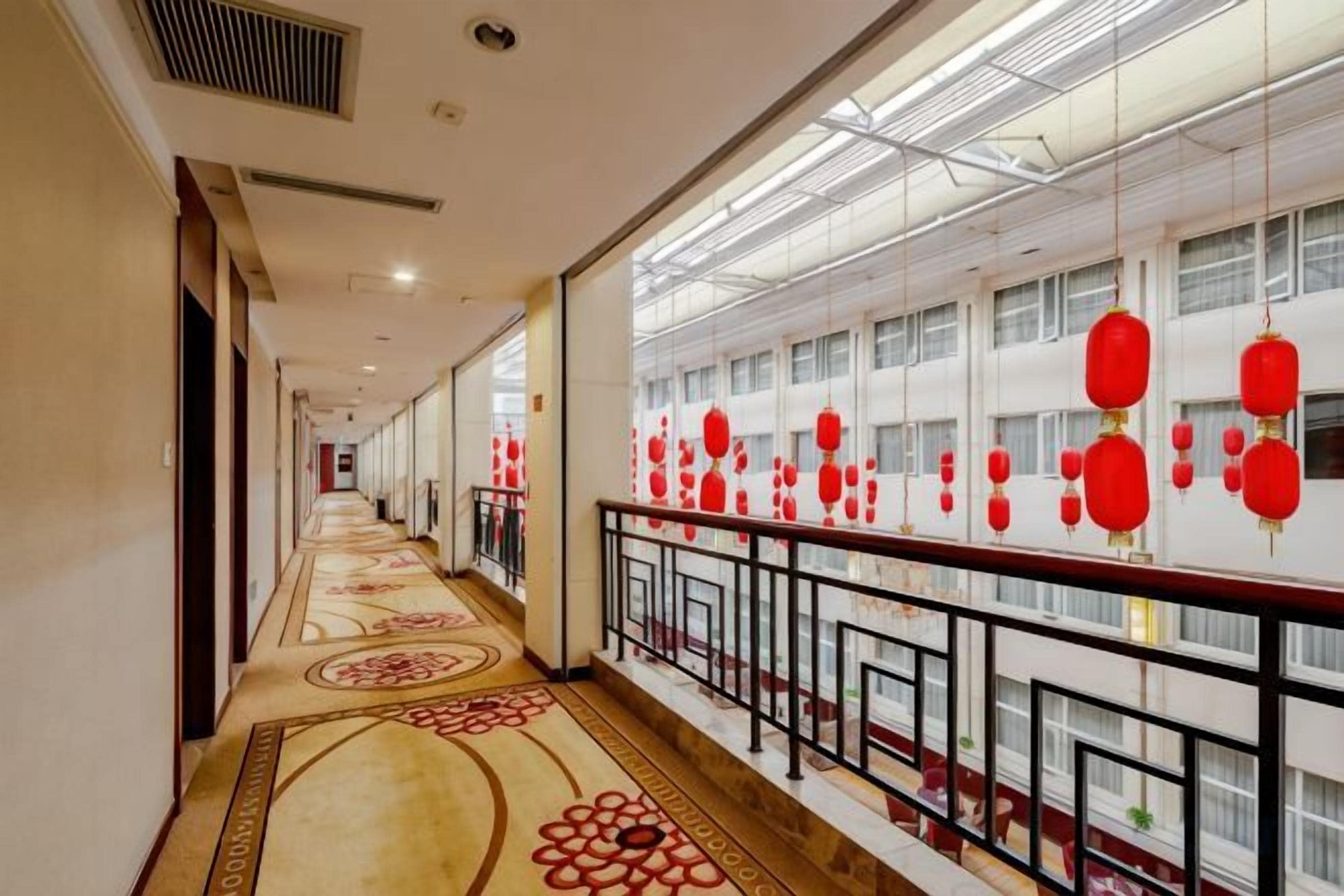 A corridor with patterned flooring, a railing, and red lanterns.