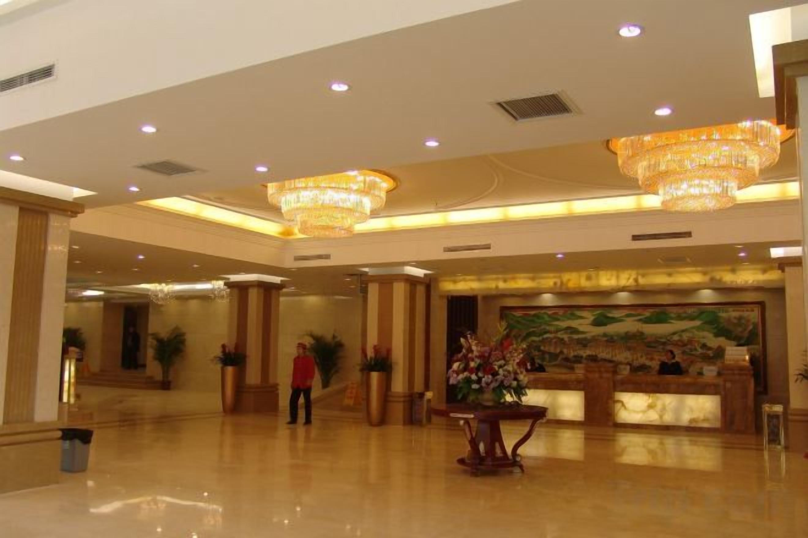 A spacious lobby with a reception desk, large chandeliers, and a mural on the wall.