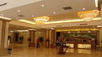 A spacious lobby with a reception desk, large chandeliers, and a mural on the wall.