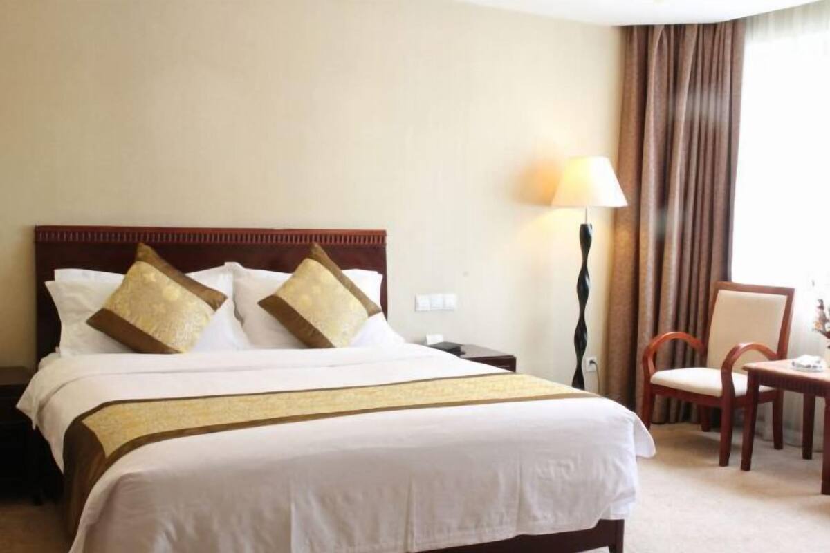 Une chambre d’hôtel avec un grand lit, une table de chevet, une lampe, une chaise et une vue sur l’extérieur.
