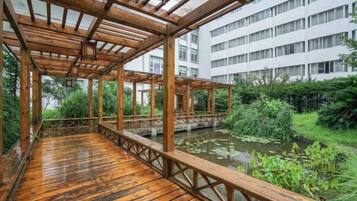 A wooden deck with a view of a pond and greenery, overlooking a multi-story building.