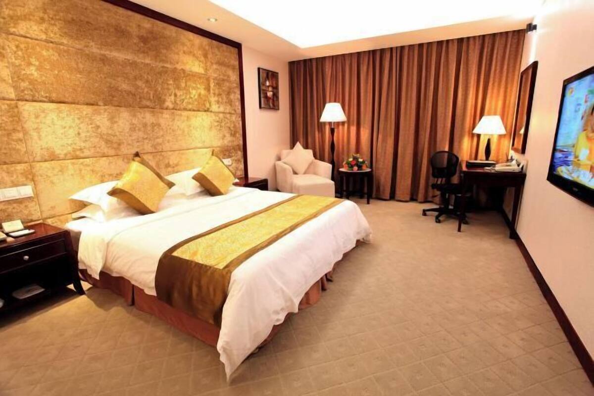 Une chambre d’hôtel avec un grand lit, un bureau, une chaise, une télévision et un rideau.