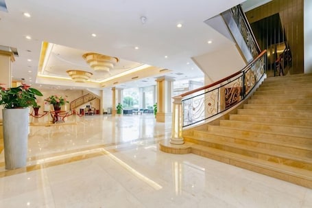 A spacious lobby with a marble floor, a staircase with a handrail, and potted plants.. East Hotel