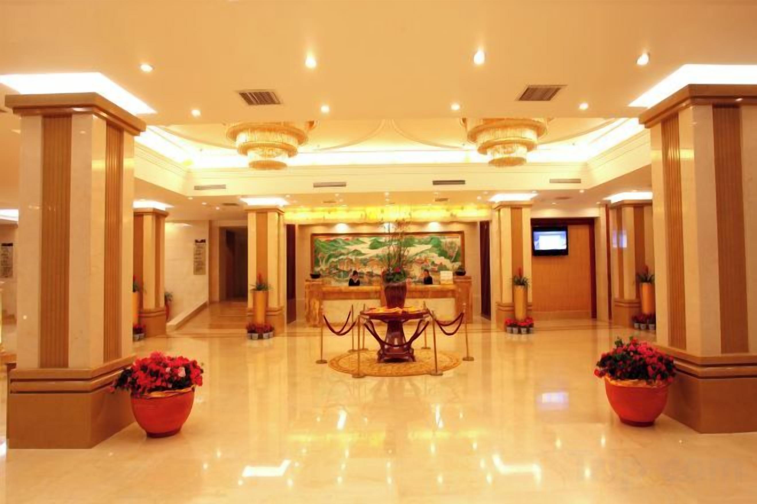 A spacious lobby with a reception desk, a large painting, and potted plants.