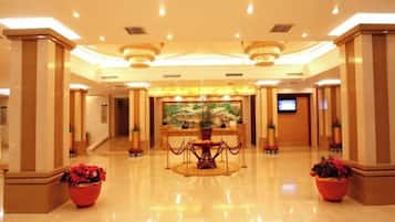 A spacious lobby with a reception desk, a large painting, and potted plants.