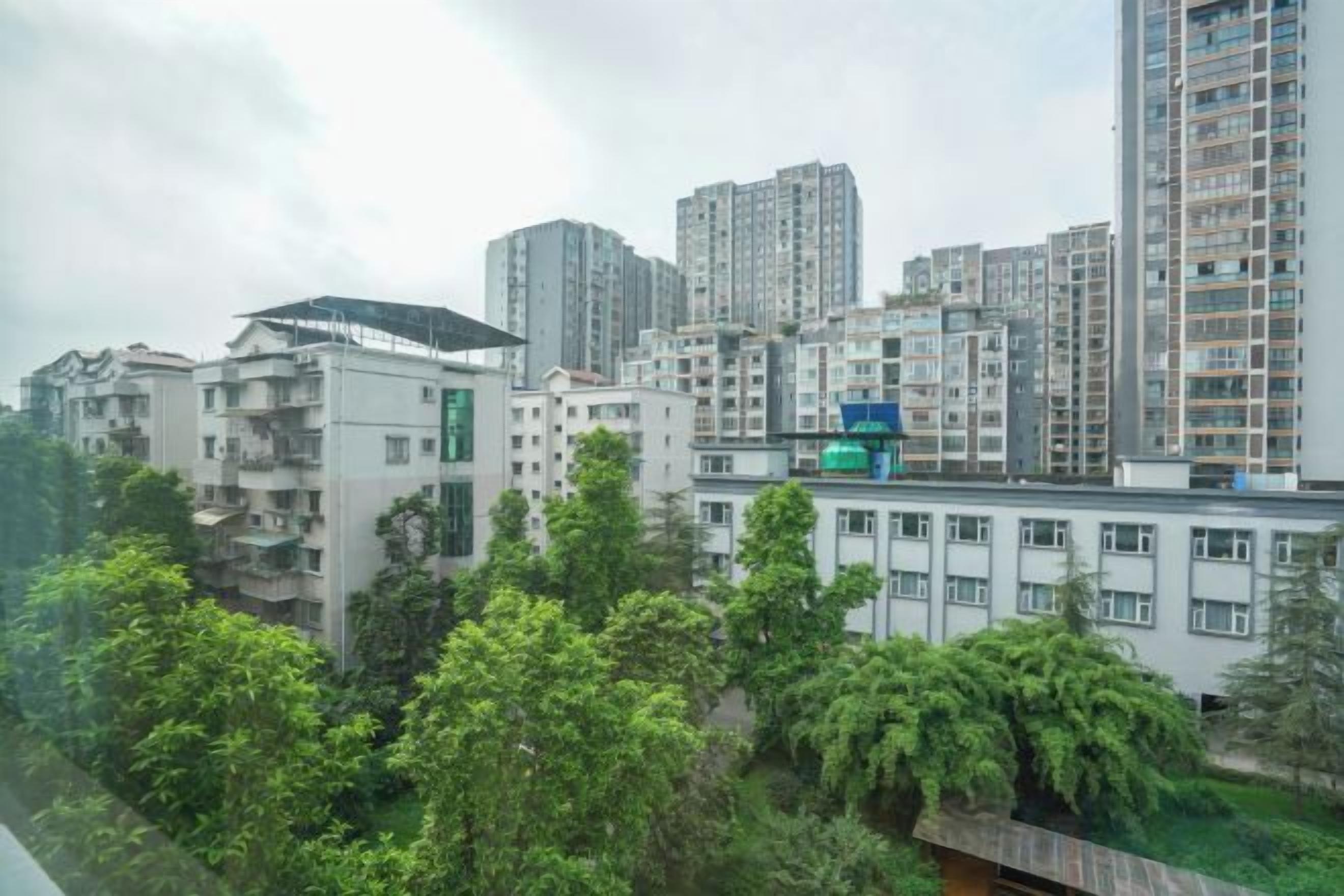 Un edificio residencial alto con varios pisos, rodeado de vegetación y otros edificios.