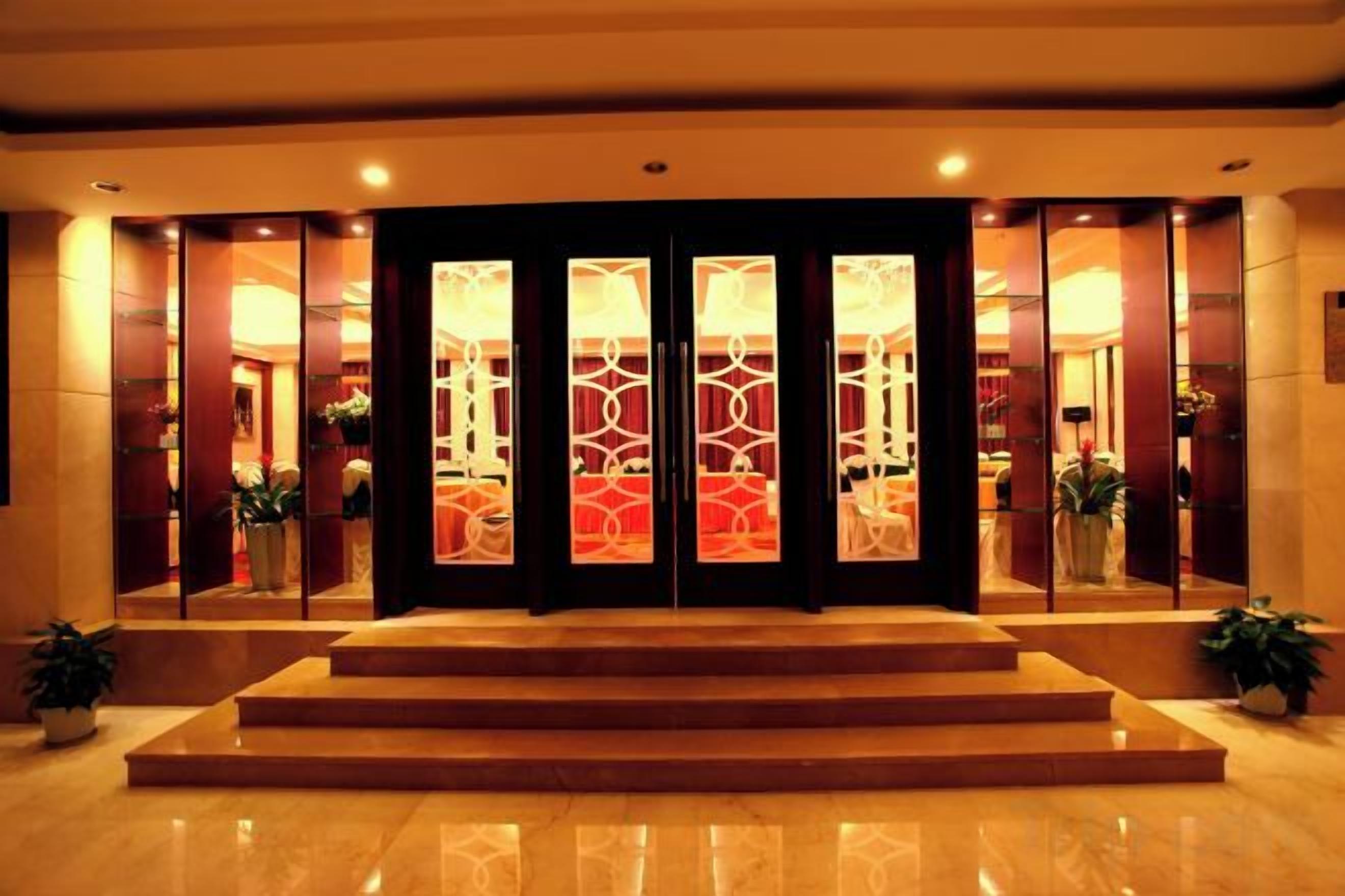 A hotel entrance with a set of double doors, a marble floor, and a small step leading up to the entrance.