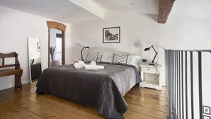 A bedroom with a large bed, wooden floor, a nightstand with a lamp, a mirror, and a picture on the wall. - A Few Steps to The Duomo Adorable 1BD Apt (Florence)