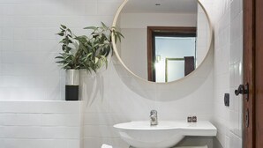 A bathroom with a white sink, a mirror, a potted plant, and a wooden shelf with towels. - A Few Steps to The Duomo Adorable 1BD Apt (Florence)