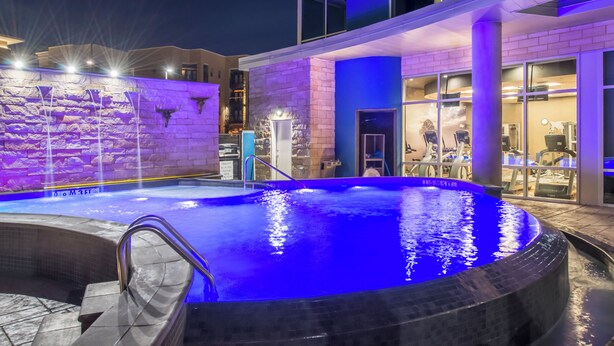 An outdoor swimming pool with a stone wall and a modern building in the background. - Hotel Indigo (Frisco)