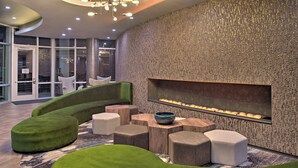 A modern lounge area with a curved green sofa, wooden side tables, and a built-in fireplace. - Hotel Indigo (Frisco)