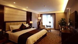 A hotel room with a large bed, a desk, a chair, a lamp, and a plant. - Jinling Netda Hotel (Nantong)