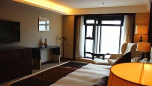 A hotel room with a large bed, a desk, a chair, a TV, and a window with curtains. - Jinling Netda Hotel (Nantong)
