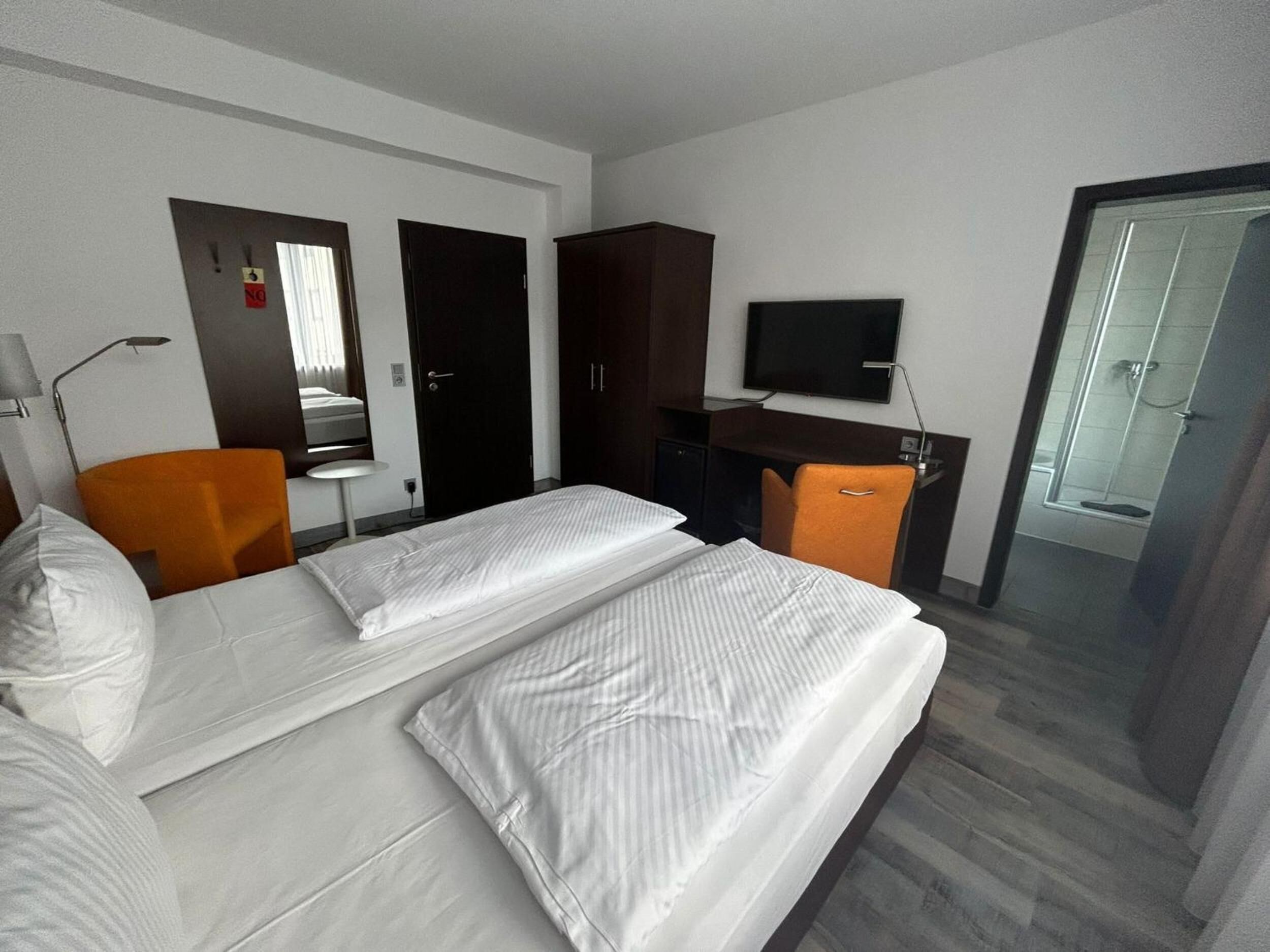 Habitación de hotel con dos camas, un escritorio, un televisor y zona de ducha.