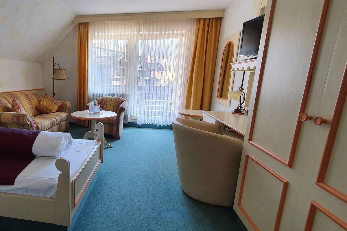 A hotel room with a bed, a sofa, a chair, a small table, and a TV.