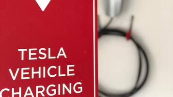 Ein rotes Schild mit einem weißen Blitz und dem Text 'TESLA VEHICLE CHARGING'.