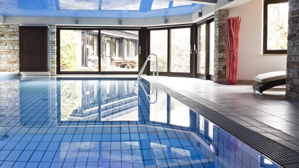 An indoor swimming pool with clear glass ceiling, stone walls, and large windows. - Kainsbacher Mühle (Happurg)