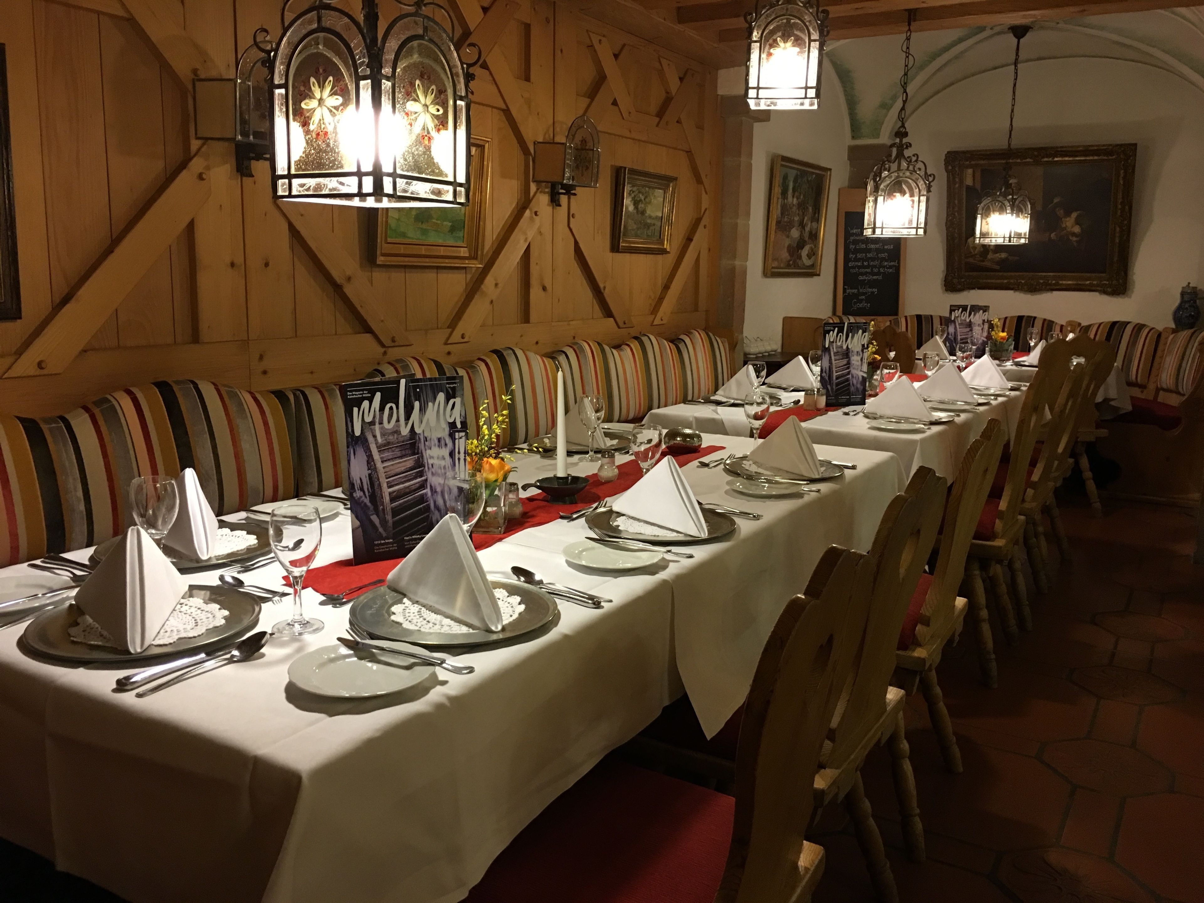 A long dining table set with white tablecloths, silverware, and red napkins.