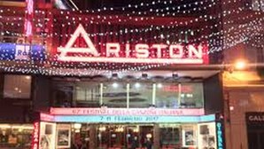 Un teatro con una pensilina che riporta la scritta "ARISTON" e un cartello per la "7a Edizione del Festival della Canzone Italiana".