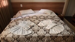 A hotel room with two beds, each with a patterned bedspread and pillows. There is a wooden headboard, a nightstand with a phone and remote control, and a window with curtains. - Hotel Itamarati (São José do Rio Preto)