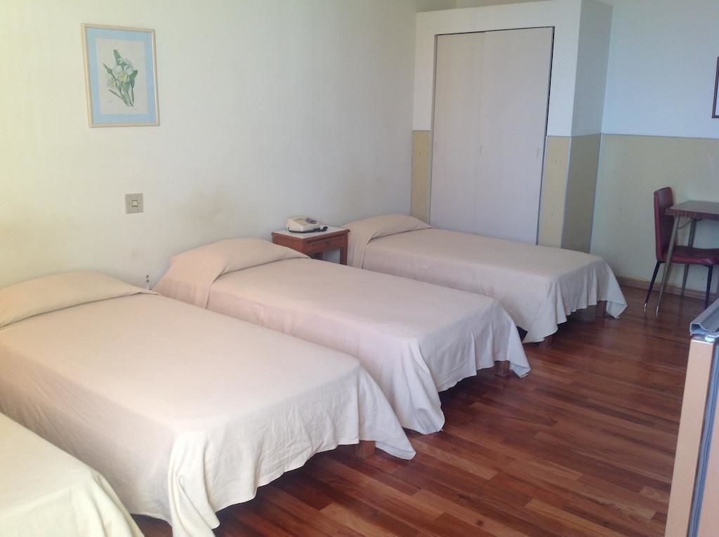 A room with three single beds, a wooden floor, a small table with a telephone, and a chair.