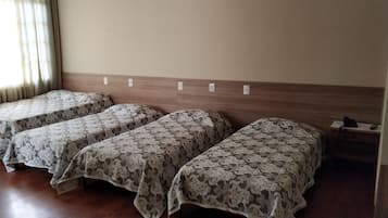 Habitación de hotel con tres camas individuales, cabecera de madera y un escritorio pequeño con teléfono.