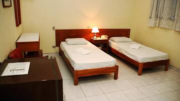A hotel room with two single beds, a desk with a chair, a lamp, and a telephone.