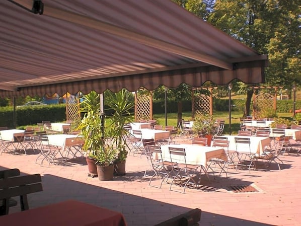 Un espace extérieur aménagé en terrasse, avec des tables et des chaises, des plantes en pot et une partie abritée.