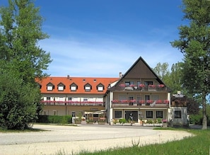 Un bâtiment à deux étages, avec un toit rouge, de nombreux balcons ornés de jardinières et une enseigne indiquant qu’il s’agit d’un restaurant.