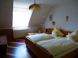A bedroom with a large bed, a bedside table, a lamp, a radiator, and a window with curtains.